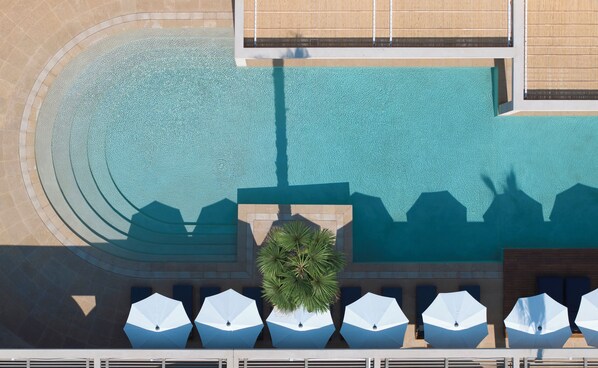 An aerial view of a pool area with a palm tree, lounge chairs, and umbrellas. - Avant Mar Paros (Paros)