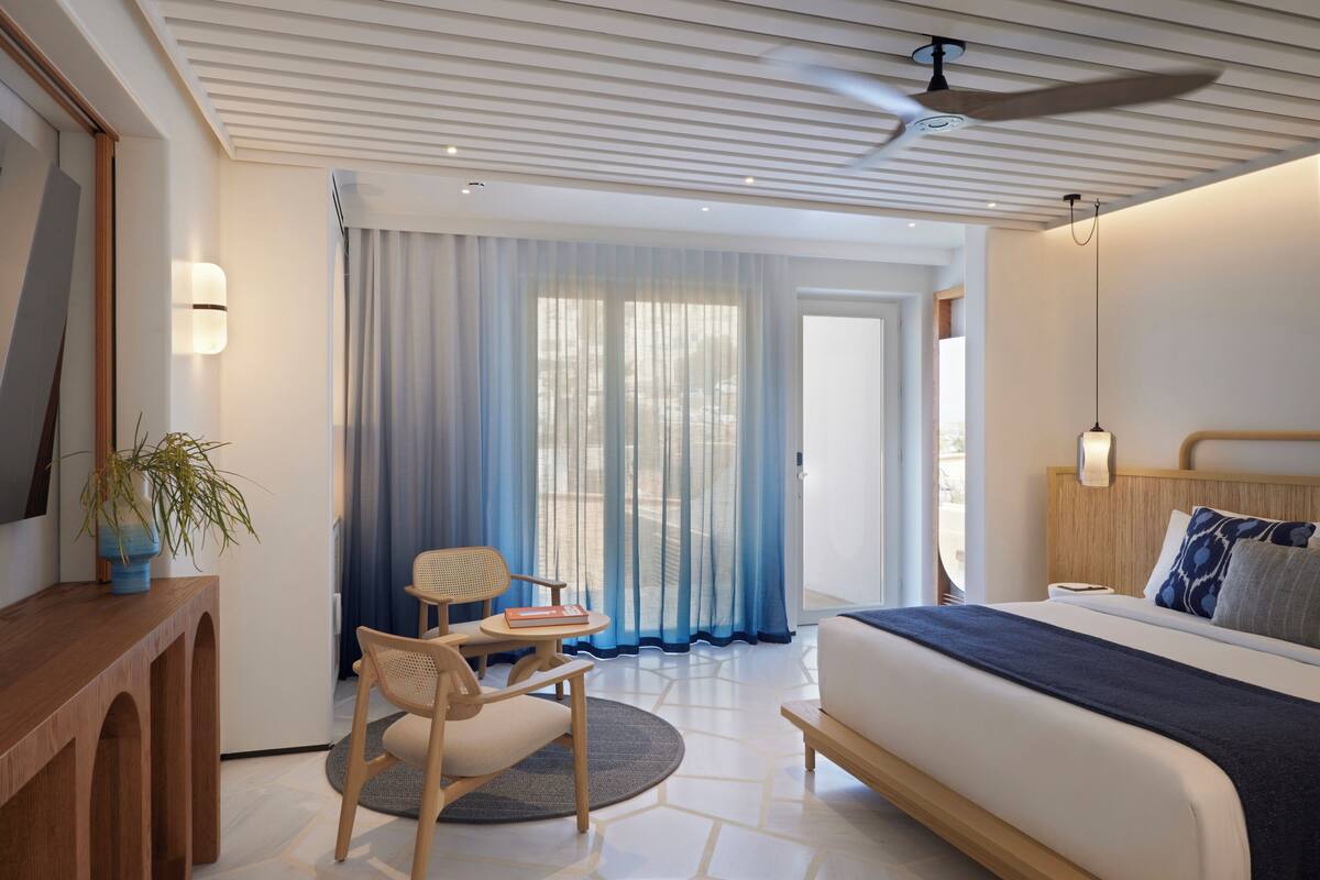 Una habitación de hotel moderna con una cama grande, un escritorio con silla, una mesita pequeña y una planta en maceta.