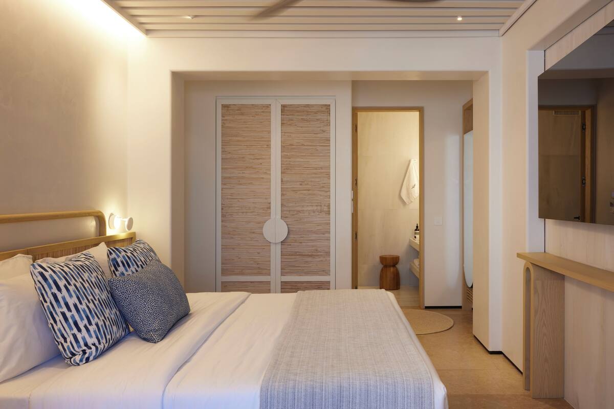 Un dormitorio moderno con cama, lámparas de noche, un armario y un taburete de madera.