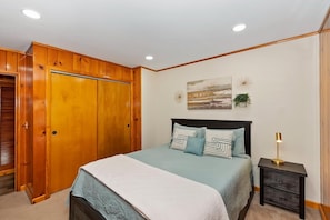 A bedroom with a bed, a nightstand, a wooden wardrobe, and a wall-mounted artwork. - Wren's Cottage by Destination Big Bear: Pet Friendly! Spa! Located in the Summit Lake Neighborhood! Infinity Game Table! Fenced Yard! Playgym! Horseshoe Pit! (Big Bear Lake)