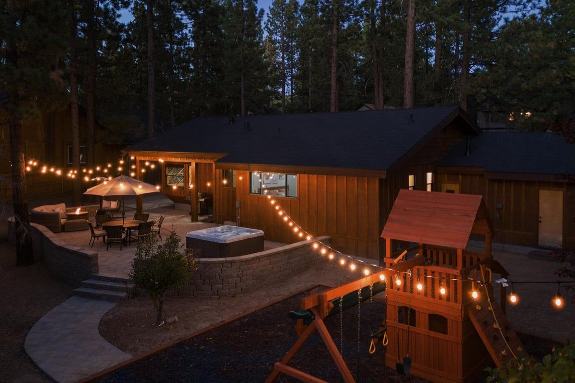 A wooden cabin with a patio, outdoor seating, a hot tub, and a play area.