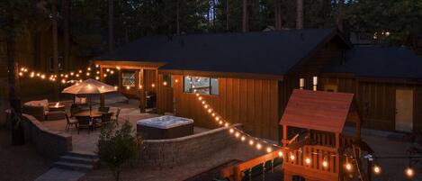 A wooden cabin with a patio, outdoor seating, a hot tub, and a play area.