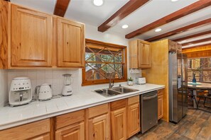 A kitchen with wooden cabinets, a stainless steel refrigerator, and a window with a wooden frame.