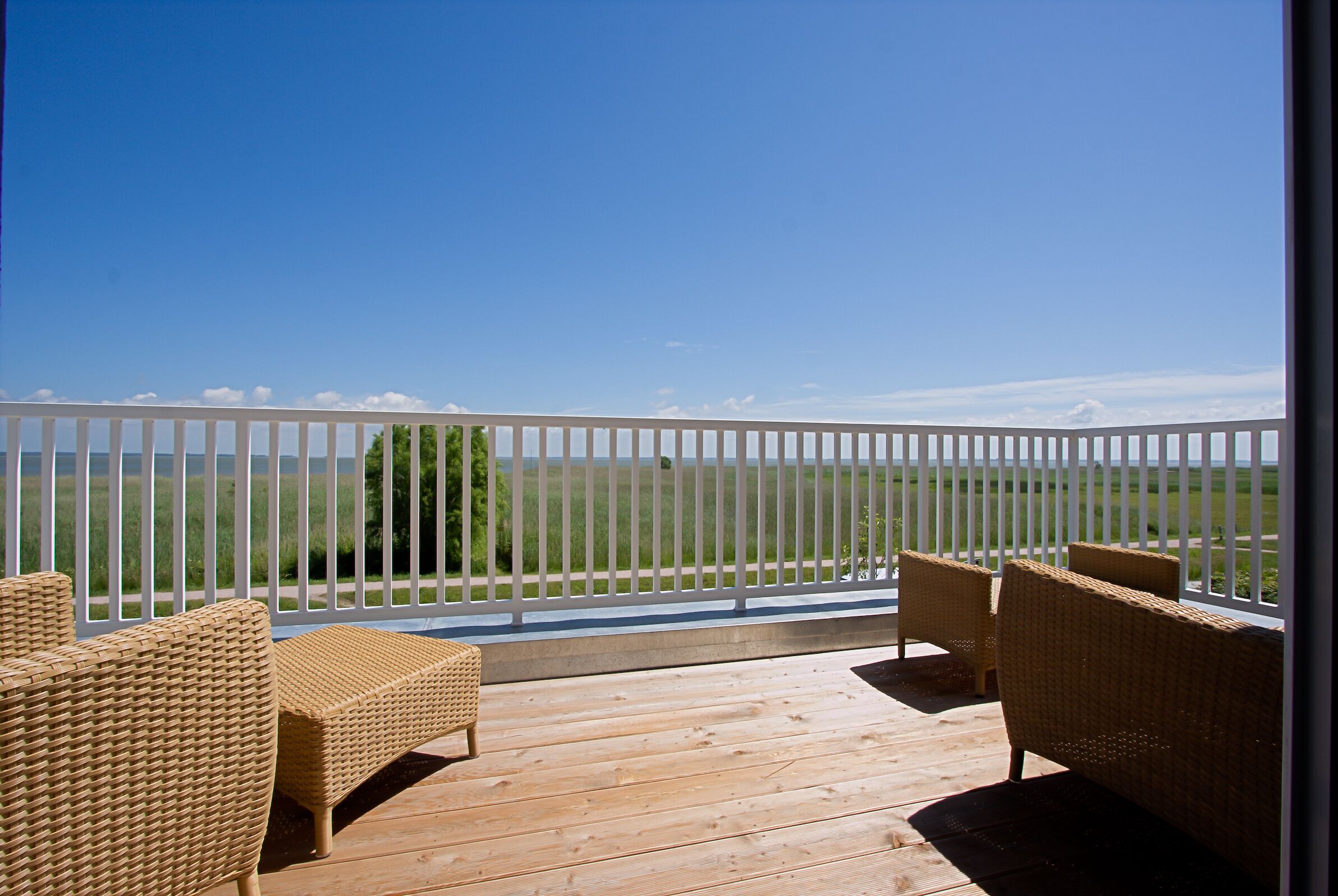 A wooden deck with wicker furniture and a white fence overlooking a grassy field.