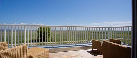 A wooden deck with wicker furniture and a white fence overlooking a grassy field.