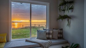A room with a large window overlooking a sunset over a grassy field. - Oceanfront Family Retreat (Oak Harbor)