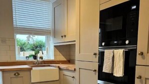 Una cocina con armarios color beige, un horno negro y una ventana con persianas.