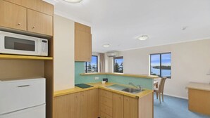Une cuisine compacte avec des meubles en bois, un four à micro-ondes, un évier et une vue sur un lac grâce à de grandes fenêtres.