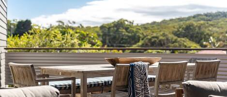Un patio al aire libre con muebles de madera, incluyendo una mesa y sillas, y vistas a un paisaje verde exuberante al fondo.