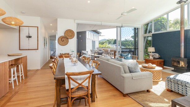 Un vaste espace de vie comprenant une longue table à manger en bois, un canapé et une grande fenêtre donnant sur l’extérieur.