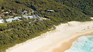 Vue aérienne d’une zone côtière comprenant une plage, une route et un ensemble de bâtiments entourés d’une forêt dense.