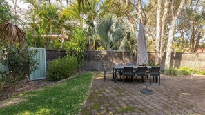 An outdoor patio with a table and chairs, surrounded by various plants and trees.