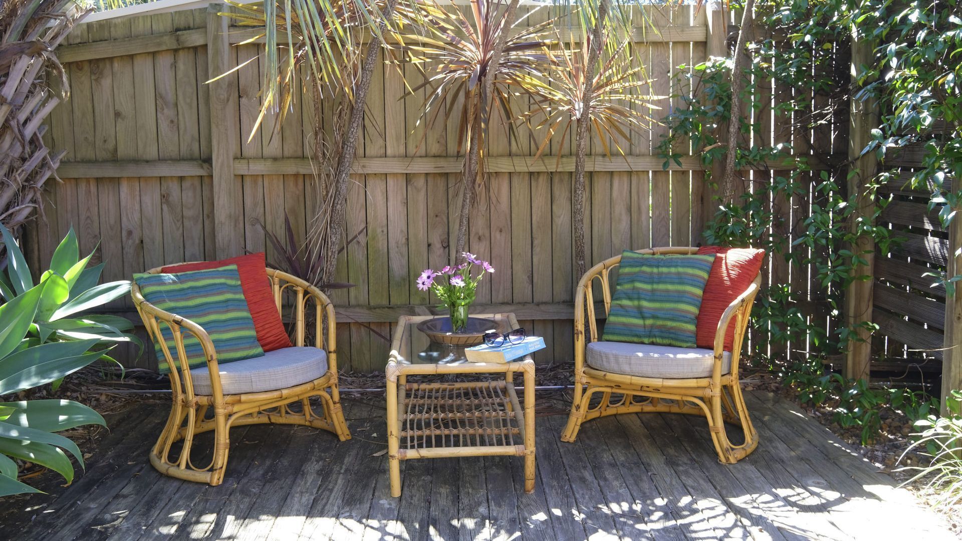 Two wicker chairs with cushions, a small table with a vase of flowers, and a wooden deck.