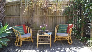 Two wicker chairs with cushions, a small table with a vase of flowers, and a wooden deck. - Acacia @ Boomerang Beach (Boomerang Beach)