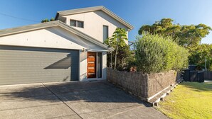 A modern two-story house with a garage, a wooden front door, and a stone wall.