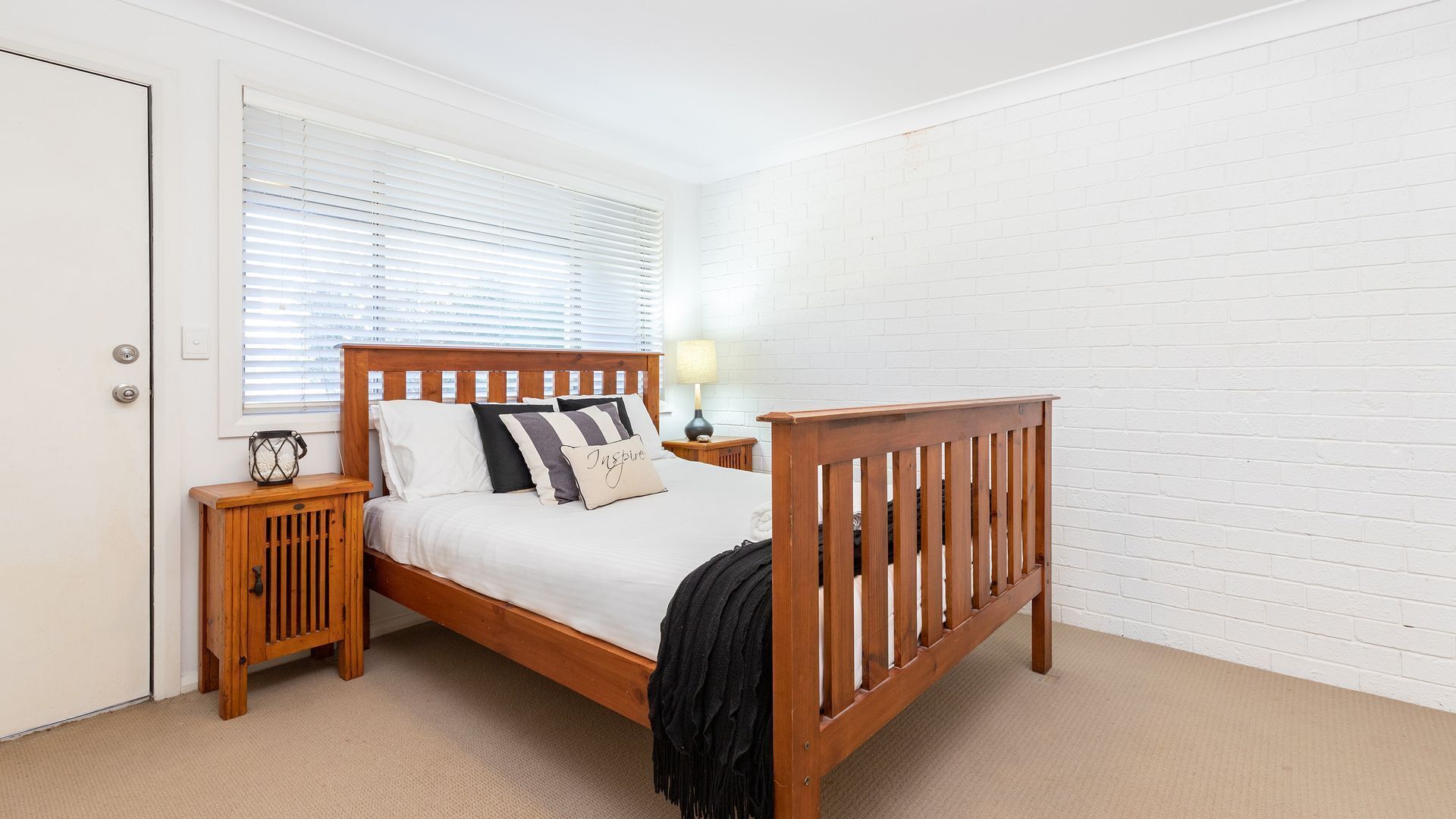 A neatly arranged bedroom with a wooden bed, a bedside table with a lamp, and a door.