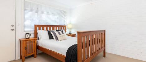 A neatly arranged bedroom with a wooden bed, a bedside table with a lamp, and a door.