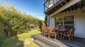 Ein modernes Haus mit einer Holzdiele, Sitzgelegenheiten im Freien und einem großen Fenster mit Blick auf einen Garten.