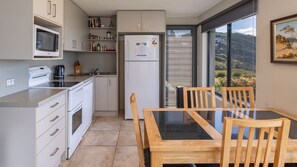 A modern kitchen with a microwave, stove, and refrigerator. There is a dining table with chairs and a window with a view of the outdoors. - @ Blueys - great for couples! (Blueys Beach)