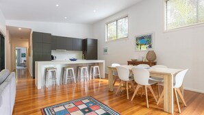 Una cocina moderna con armarios oscuros, una isla central con taburetes y una zona de comedor con mesa de madera y sillas blancas.