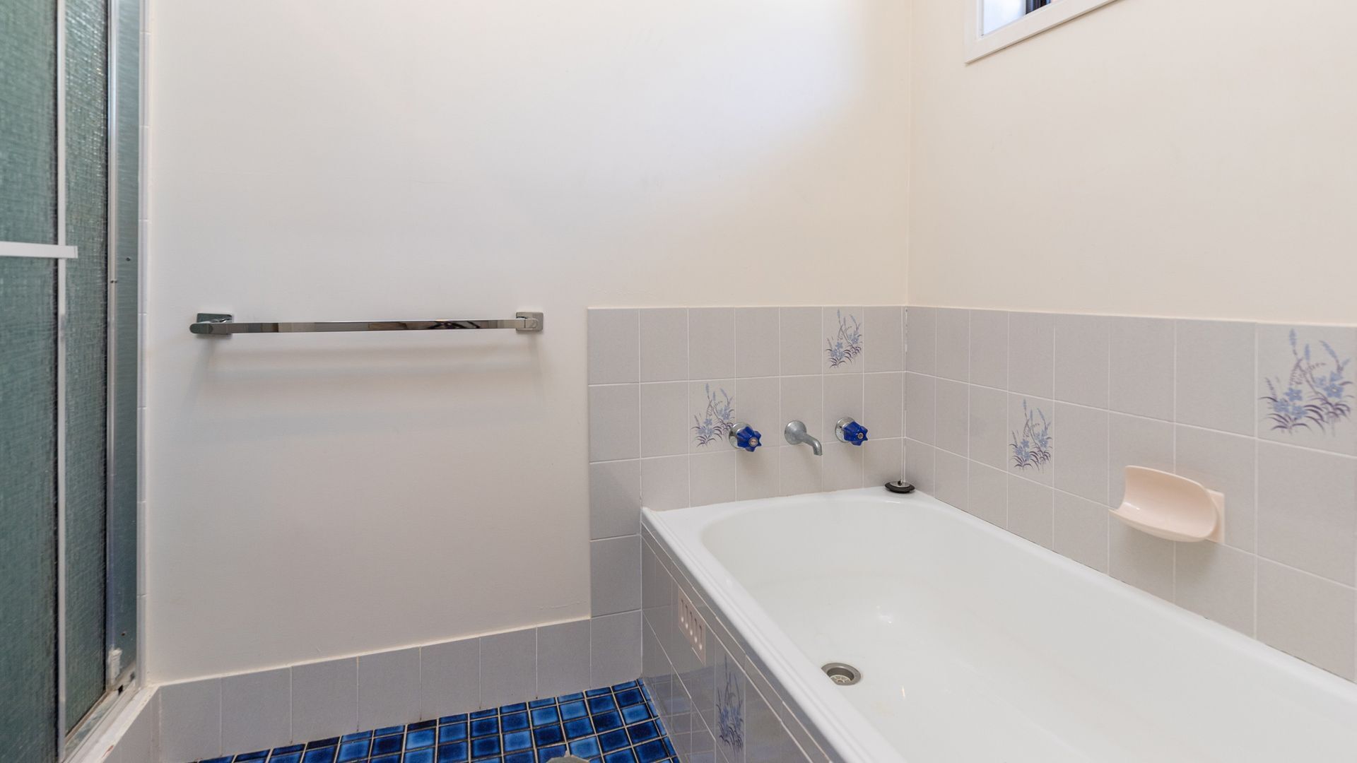 Ein Badezimmer mit einer Badewanne, einer Haltestange und dekorativen Fliesen.