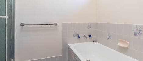 Ein Badezimmer mit einer Badewanne, einer Haltestange und dekorativen Fliesen.