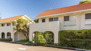 A row of two-story buildings with red-tiled roofs, numbered 17 and 18, featuring arched windows and a small patio area with chairs and plants.