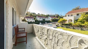 A balcony with a wooden bench, a stone wall, and a view of residential buildings in the background.