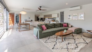 A modern living room with a sectional sofa, a dining table, and a kitchen in the background. - Boof's at Blueys Beach (Blueys Beach)