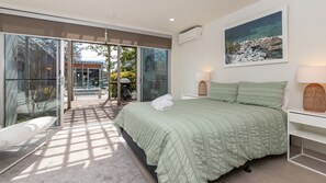 Un dormitorio con una cama grande, un ventanal de vidrio que da a un espacio exterior y un cuadro en la pared.