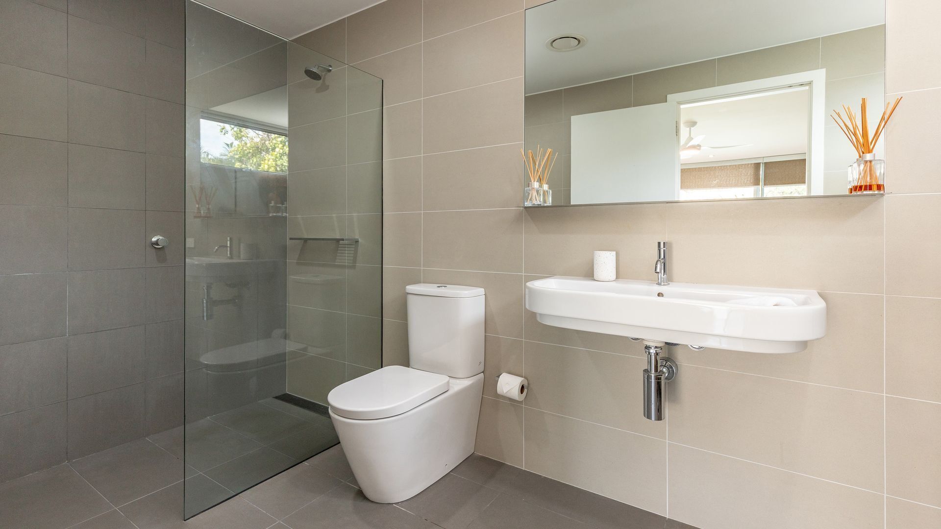 Un baño moderno con cabina de ducha de vidrio, inodoro, lavamanos y espejo.