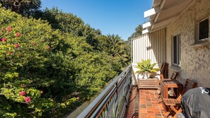 Enjoy the serene views of lush greenery from your balcony, featuring a potted plant and comfortable seating.