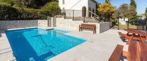 Relax by the pool surrounded by lush vegetation and a stone wall.