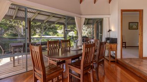 A dining area with a wooden table and chairs, large windows, and a view of the outdoors.