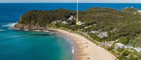 A coastal area with a beach, a lighthouse, and a hill with buildings.