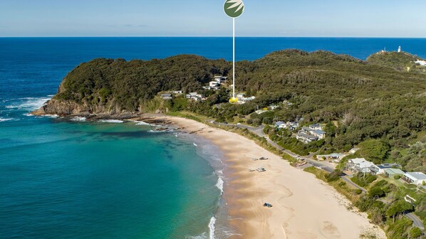 A coastal area with a beach, a lighthouse, and a hill with buildings.