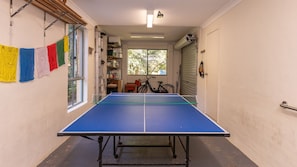A narrow hallway with a ping pong table in the center, a bicycle, and a window with a view of trees.