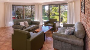 A spacious living area with a sofa set, a coffee table, and a view of a garden through large windows.