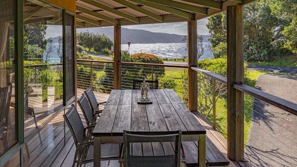 A wooden deck with a table and chairs, overlooking a scenic view of a body of water and greenery. - Far Shore @ Seal Rocks (Seal Rocks)