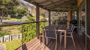 A wooden deck with a table and chairs, overlooking a landscaped area with trees and a road. - Far Shore @ Seal Rocks (Seal Rocks)