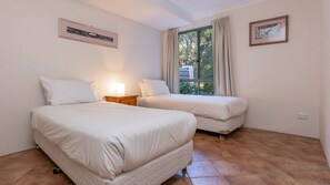 A bedroom with two beds, a nightstand, a window with curtains, and two framed pictures on the wall.