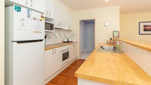 A compact kitchen with white cabinets, a built-in oven, a microwave, and a wooden countertop. - Point Break @ Boomerang Point (Boomerang Beach)