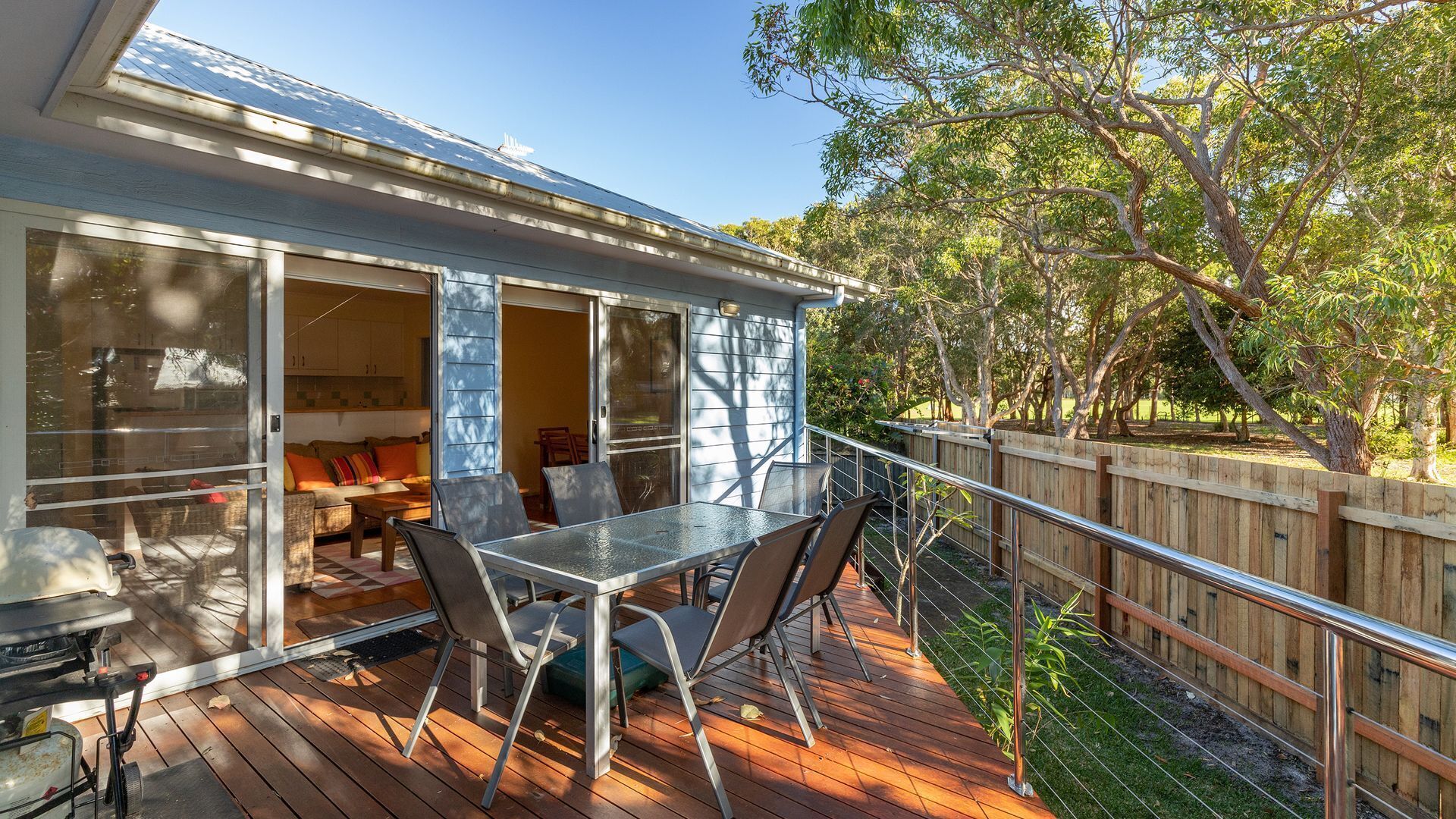 A deck with a table and chairs, a sliding glass door leading to a living area, and a wooden fence surrounding the deck.