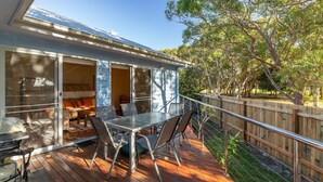 A deck with a table and chairs, a sliding glass door leading to a living area, and a wooden fence surrounding the deck. - Point Break @ Boomerang Point (Boomerang Beach)