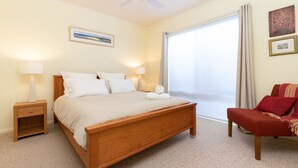 A neatly arranged bedroom with a wooden bed, bedside lamps, a chair, and a large window with curtains. - Point Break @ Boomerang Point (Boomerang Beach)