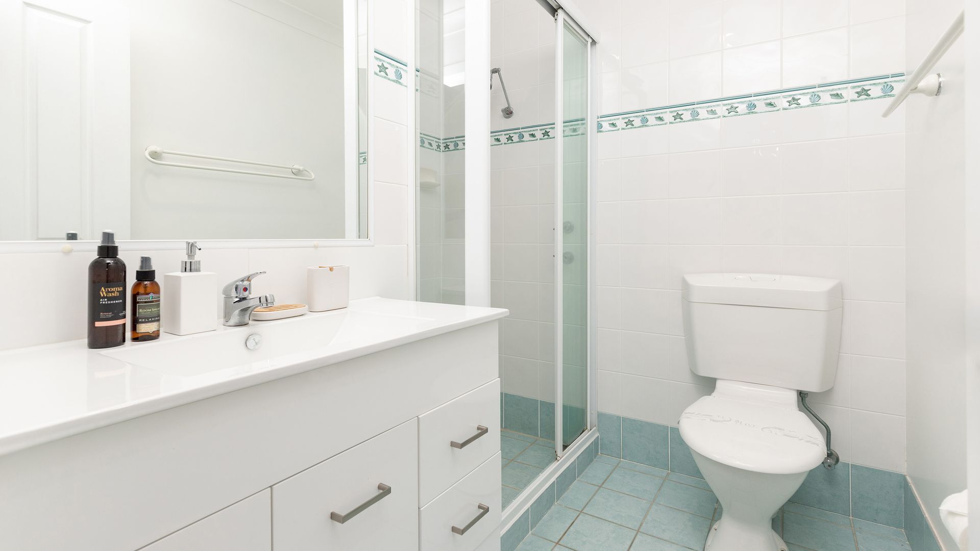 Ein Badezimmer mit einem weißen Waschbecken, zwei Seifenspenden, einem Spiegel, einer Duschkabine aus Glas und einer Toilette.