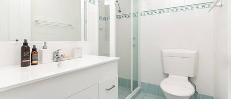 Ein Badezimmer mit einem weißen Waschbecken, zwei Seifenspenden, einem Spiegel, einer Duschkabine aus Glas und einer Toilette.
