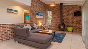 A cozy living room with a brick wall, a sofa, a coffee table, a fireplace, and artwork on the walls. - Splash @ Elizabeth Beach (Elizabeth Beach)