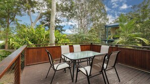 An outdoor deck with a glass-top table and four chairs, surrounded by a wooden fence and lush greenery. - Splash @ Elizabeth Beach (Elizabeth Beach)