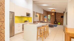 A modern kitchen with a central island, a dining area with a wooden table, and a living space with a fireplace. - Splash @ Elizabeth Beach (Elizabeth Beach)